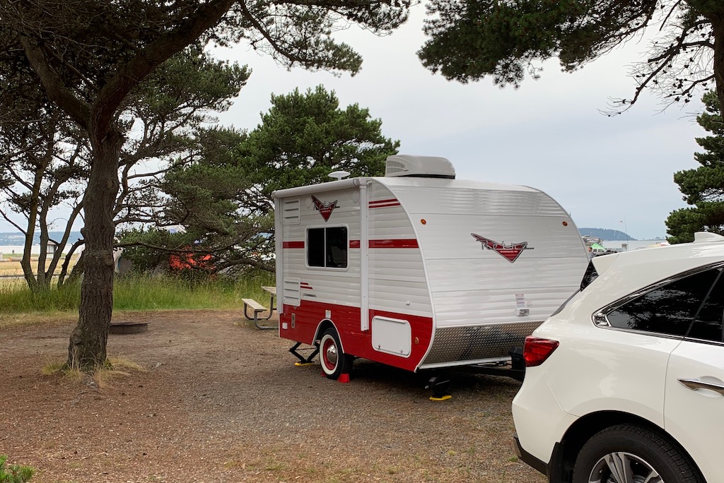 Red and white Riverside Retro 135 camper trailer parked in a tree-shaded camping spot